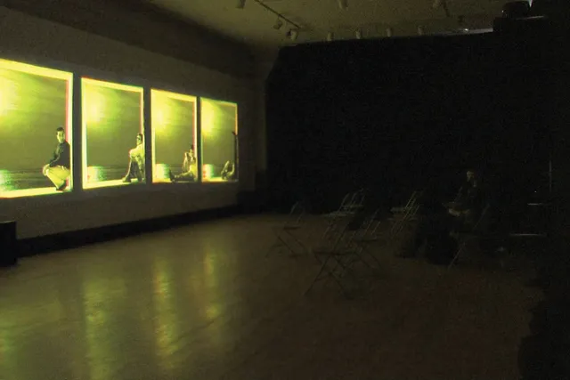 Four yellow projections of four people sitting against the wall within the box of each projection on a gallery wall. 