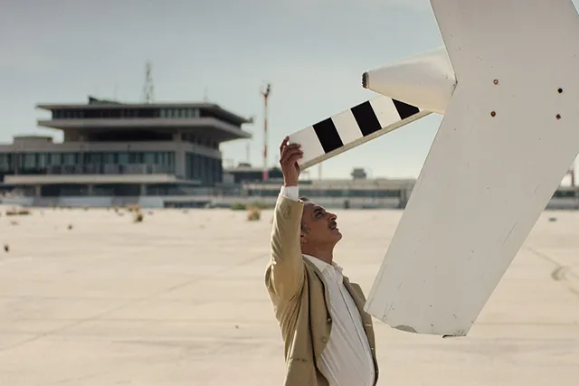 A lebanese man standing on a runway with his hand on a white helicopter rear propeller.
