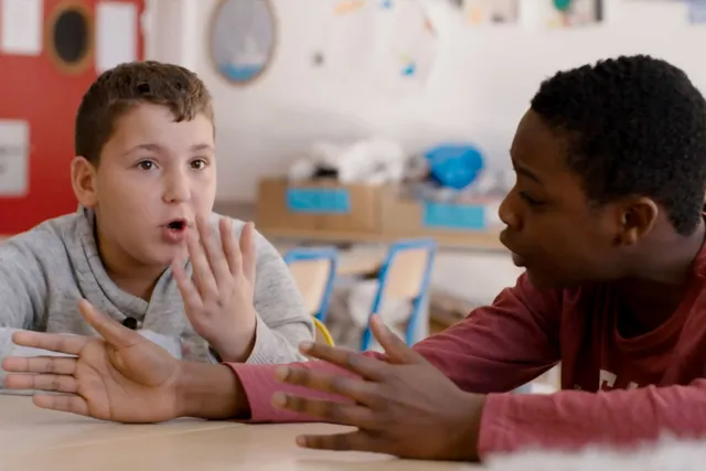 Two young boys seating in an elementary school classroom in active and animated discussion.