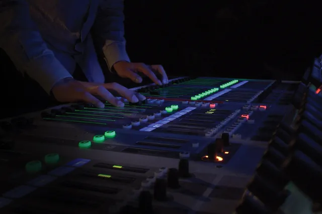 Masculine hands on a soundboard in a dark room with dim blue light. 