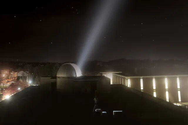 a beam of light coming out of an observatory overlooking the RPI campus at night.