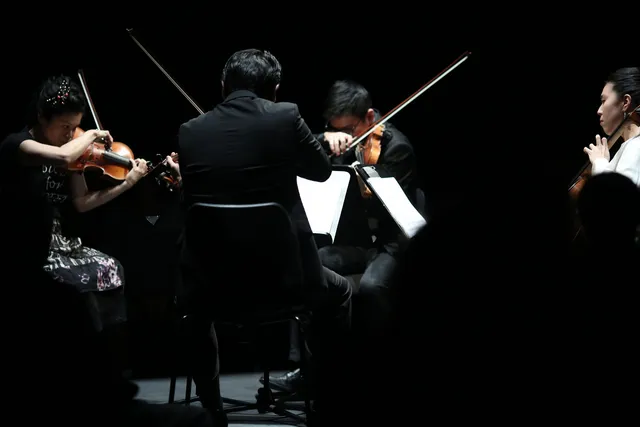Formosa Quartet actively playing in concert under a spotlight on a dark stage.