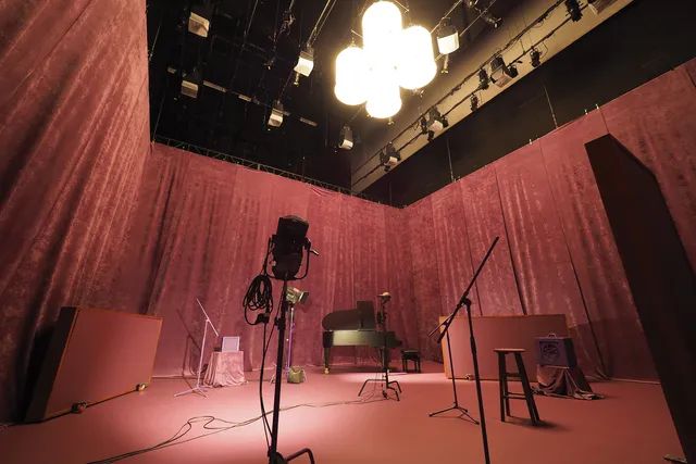 Studio set up with a piano, microphones, amp, and various lighting in a room with pink velvet walls with matching pink floors
