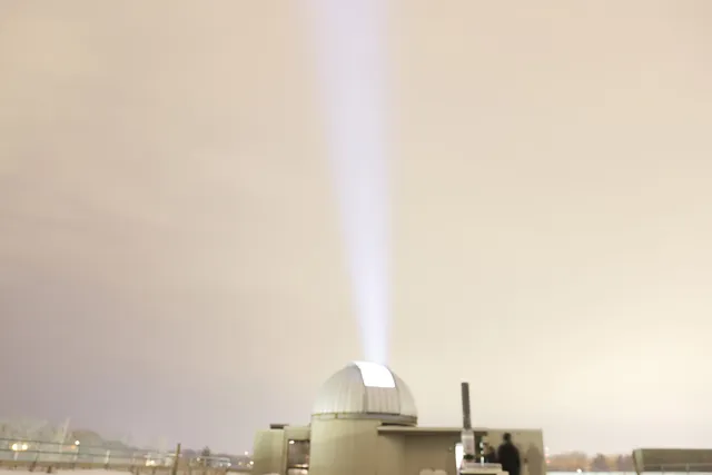 An observatory shooting a beam of light into a gray hazy sky. 