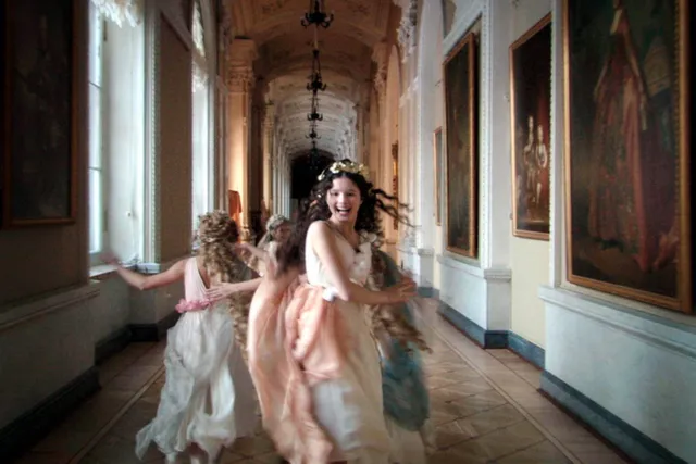 Women dressed as nymphs with flower crowns and flowing draped clothing running down the hall, burred in motion and with expressions of joy of the Hermitage in Saint Petersburg, Russia.  