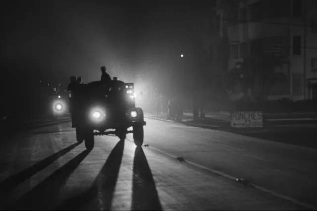 A model T on a road lit only by headlights behind it casting long shadows.