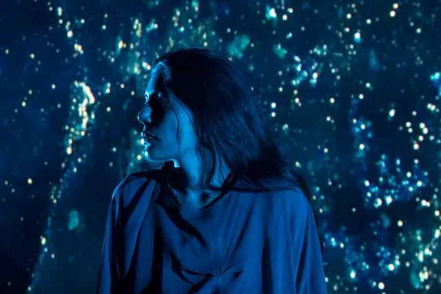 An Iranian woman stands agains a background of star-like blue light.