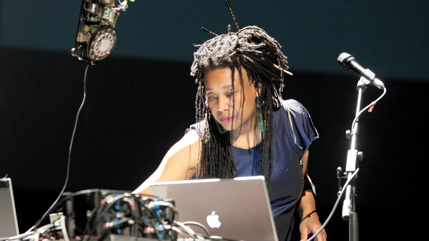 PamelaZ reaching across a lap top next to a microphone focused on the task in front of her.