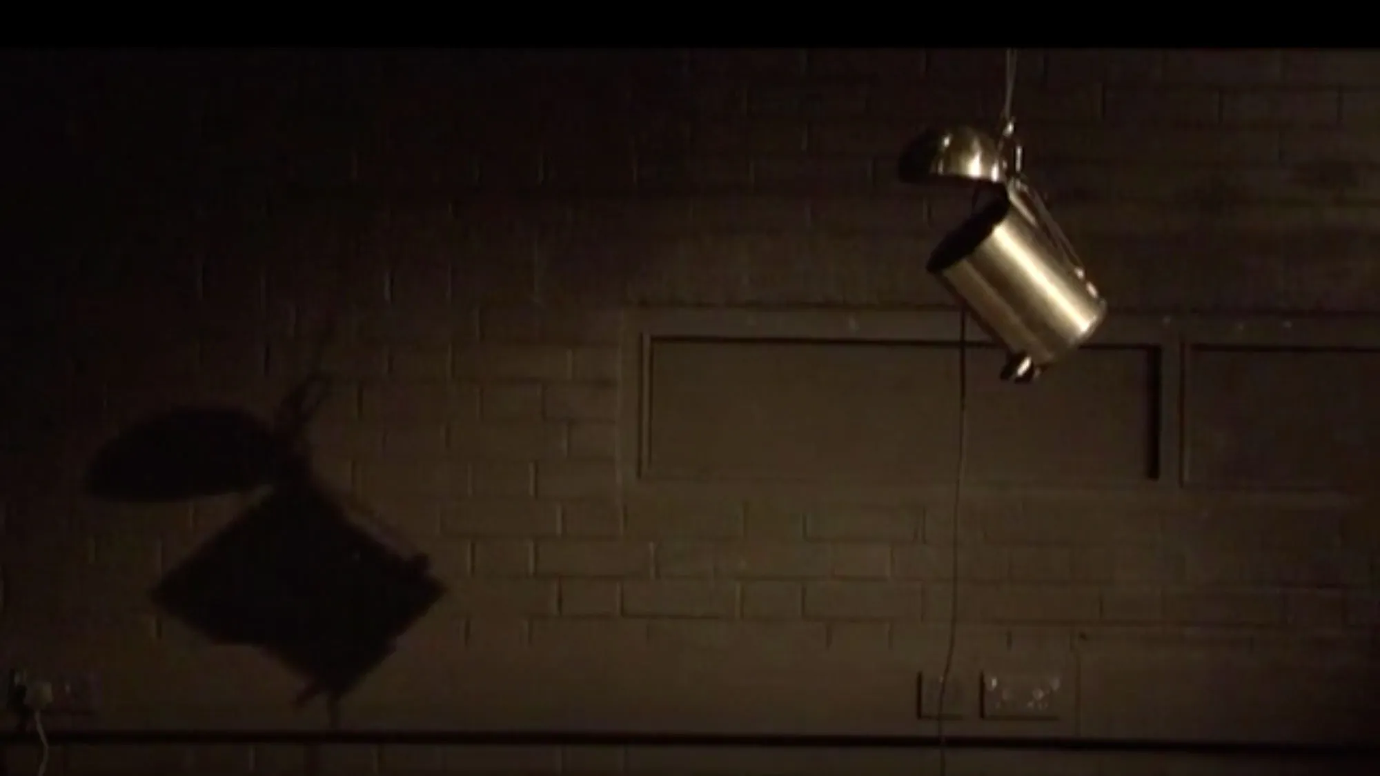 a small silver trash can hangs from a ceiling in a dark studio