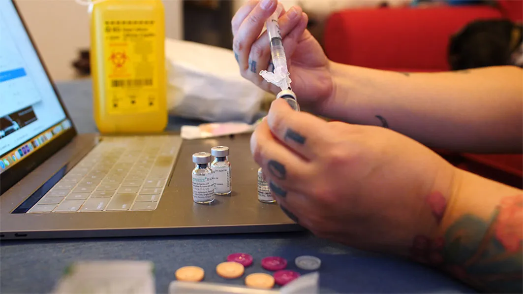 two hands withdrawing liquid from a vial with a syringe