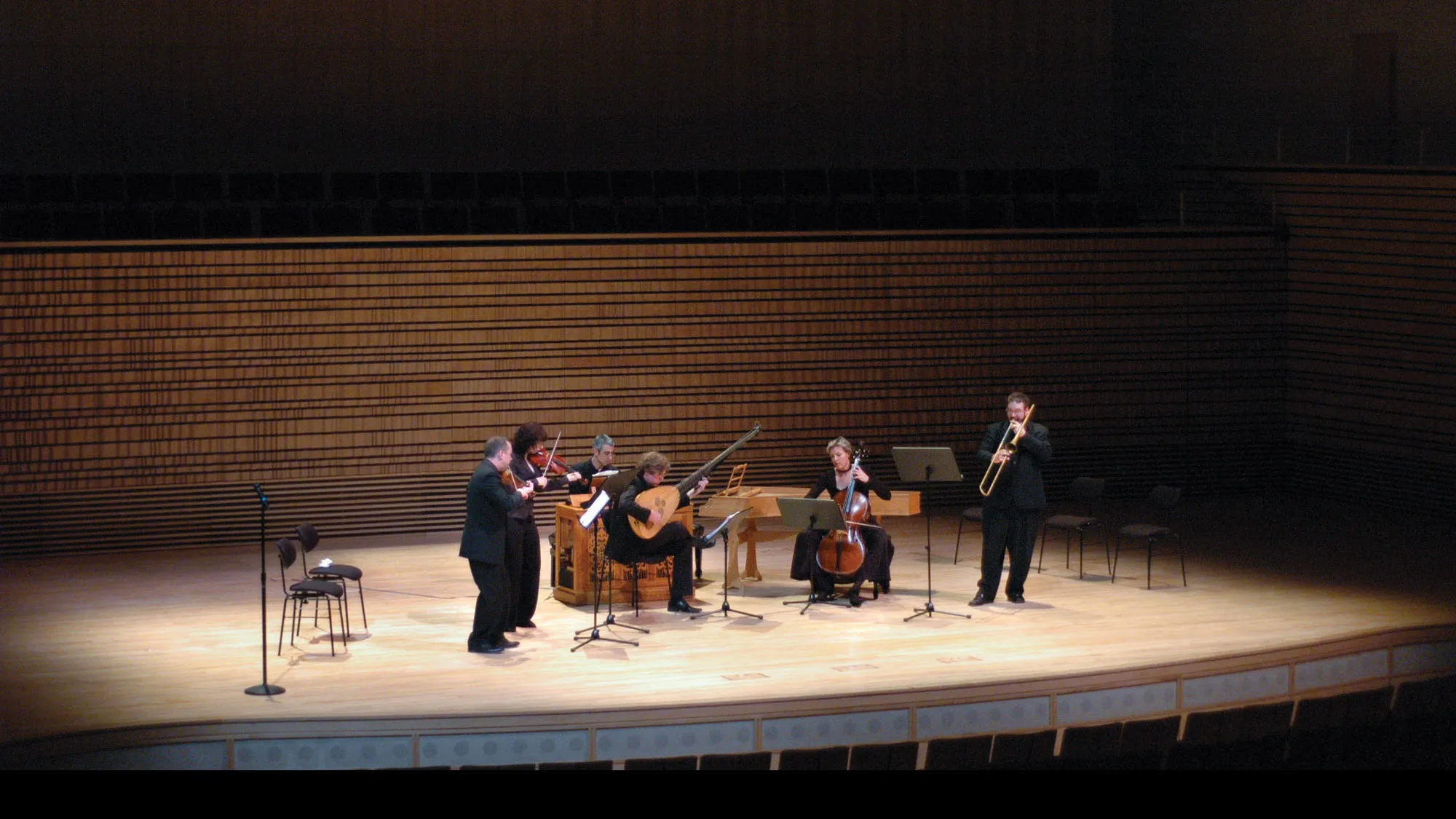 A small orchestra gathering in the middle of the concert hall stage playing in concert. 