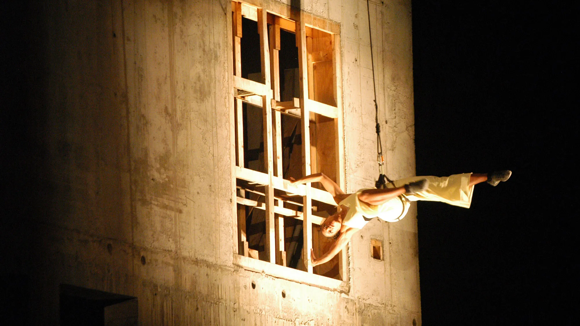 A female dancer suspended via a harness off the side of a building facade during EMPAC's construction. 