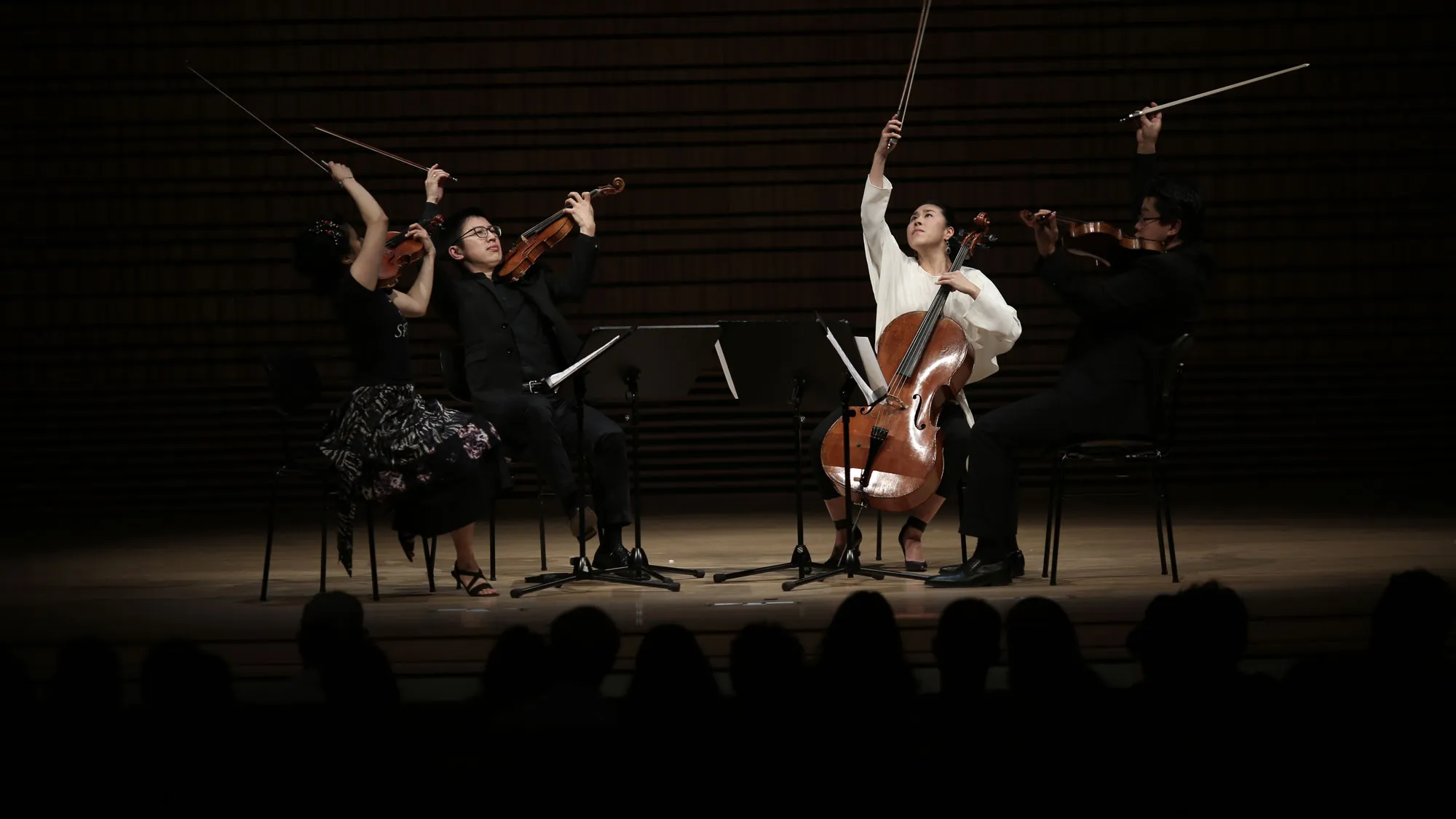 Formosa Quartet with bows lifted and pointed to the ceiling on a dimly lit concert hall stage.