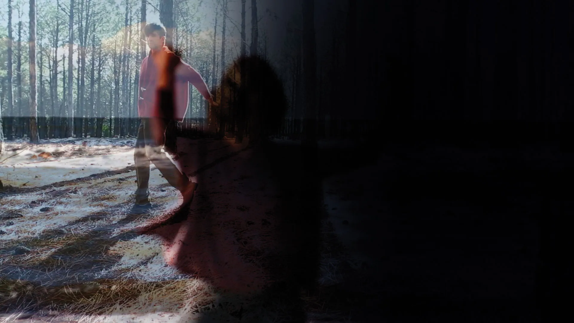 A double exposed image of a shadow of a woman reaching and a man wearing a red jacket walking through a sun dappled forest.