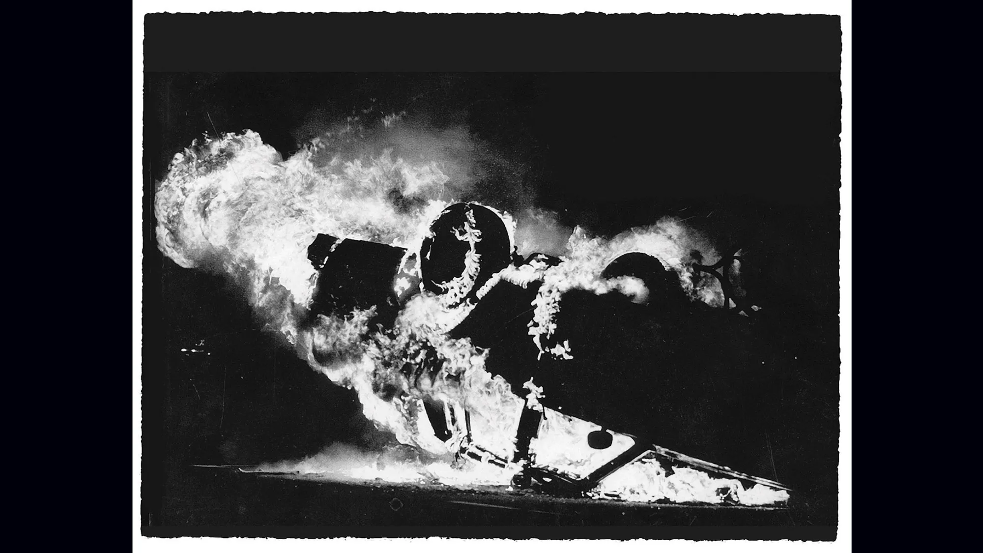 A car engulfed in flames, flipped on its back.